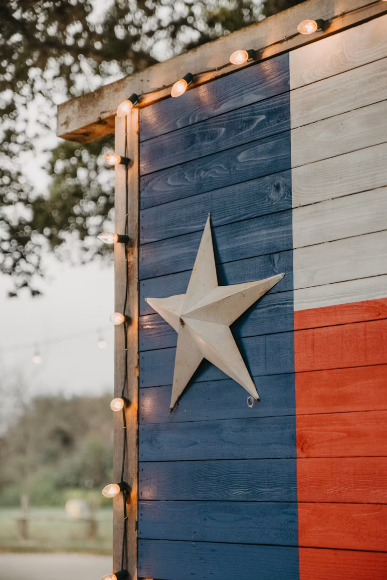 A wooden Texas flag wall with a white star and string lights.