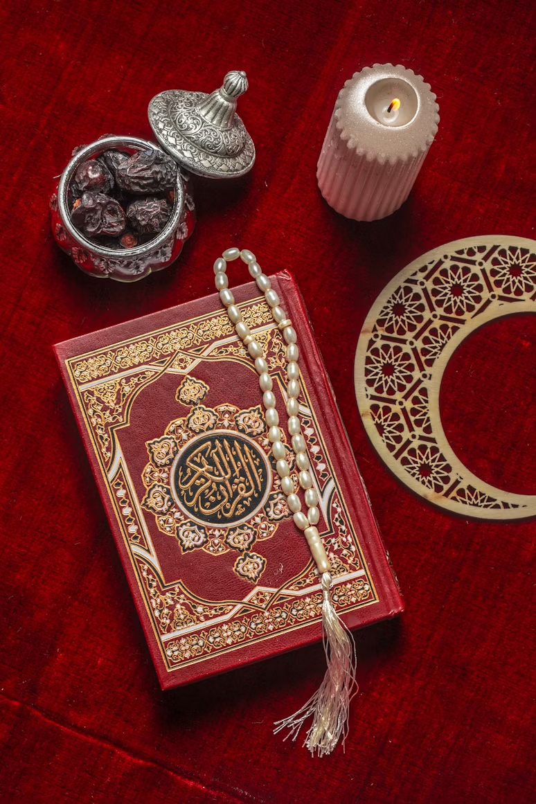 A red Qur'an with prayer beads, dates, a candle and crescent-shaped decoration on red cloth.