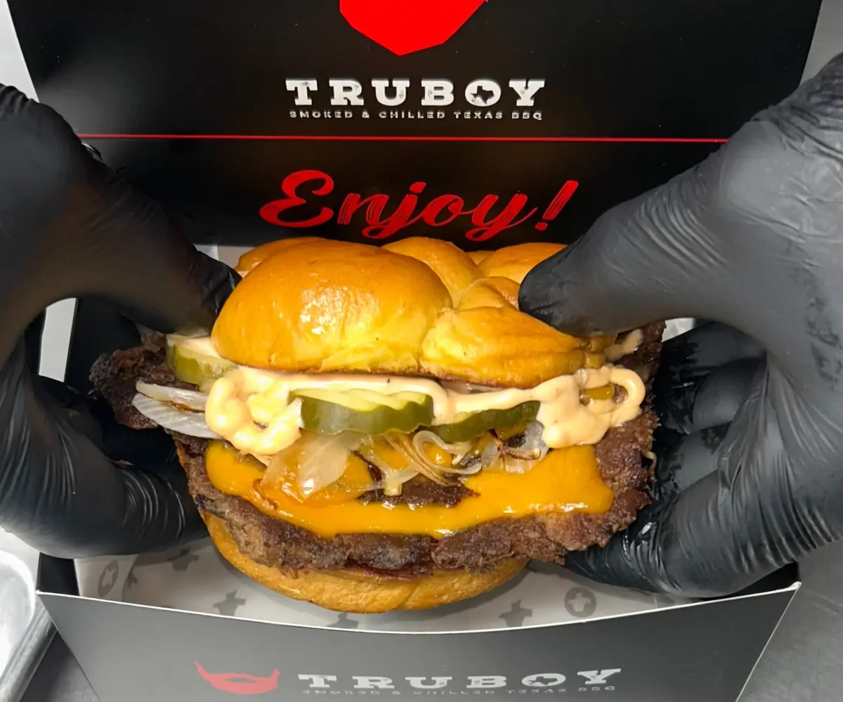 A brisket burger held over a Truboy BBQ serving box.