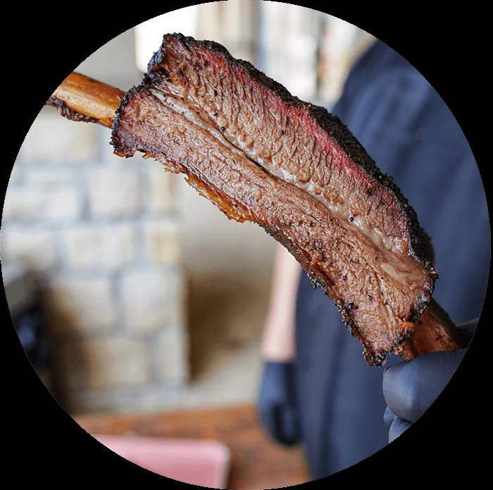 A smoked beef rib held in front of a stone wall.