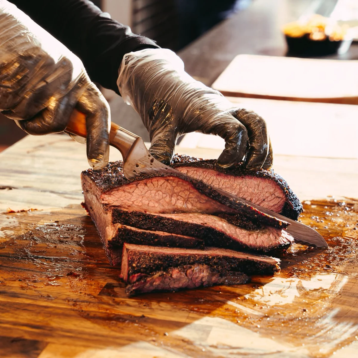 Gloved hands slicing smoked brisket on a wooden cutting board at Levant BBQ.