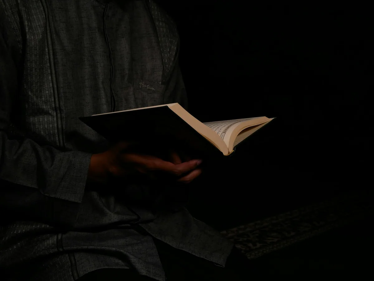 A person's torso and hands holding an open book in low light.