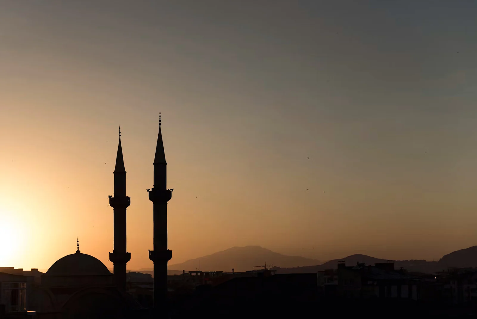 Mosque minarets silhouetted against a warm sunset sky.