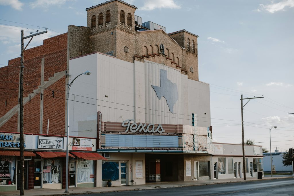 An older brick theatre building with a marquee reading Texas, seen along a quiet small-town street.